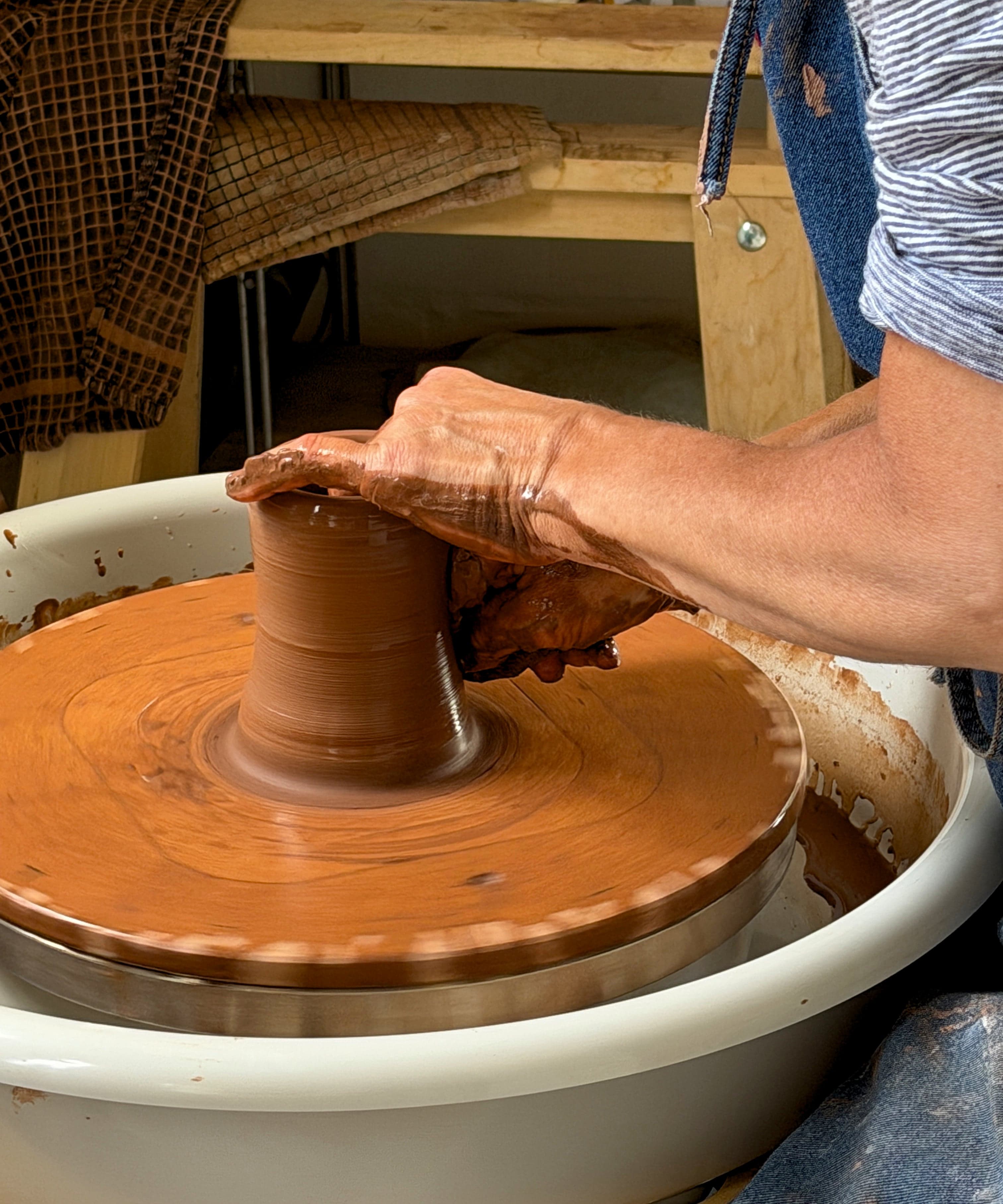 Hands cupped around red terracotta being centred on the spinning wheel