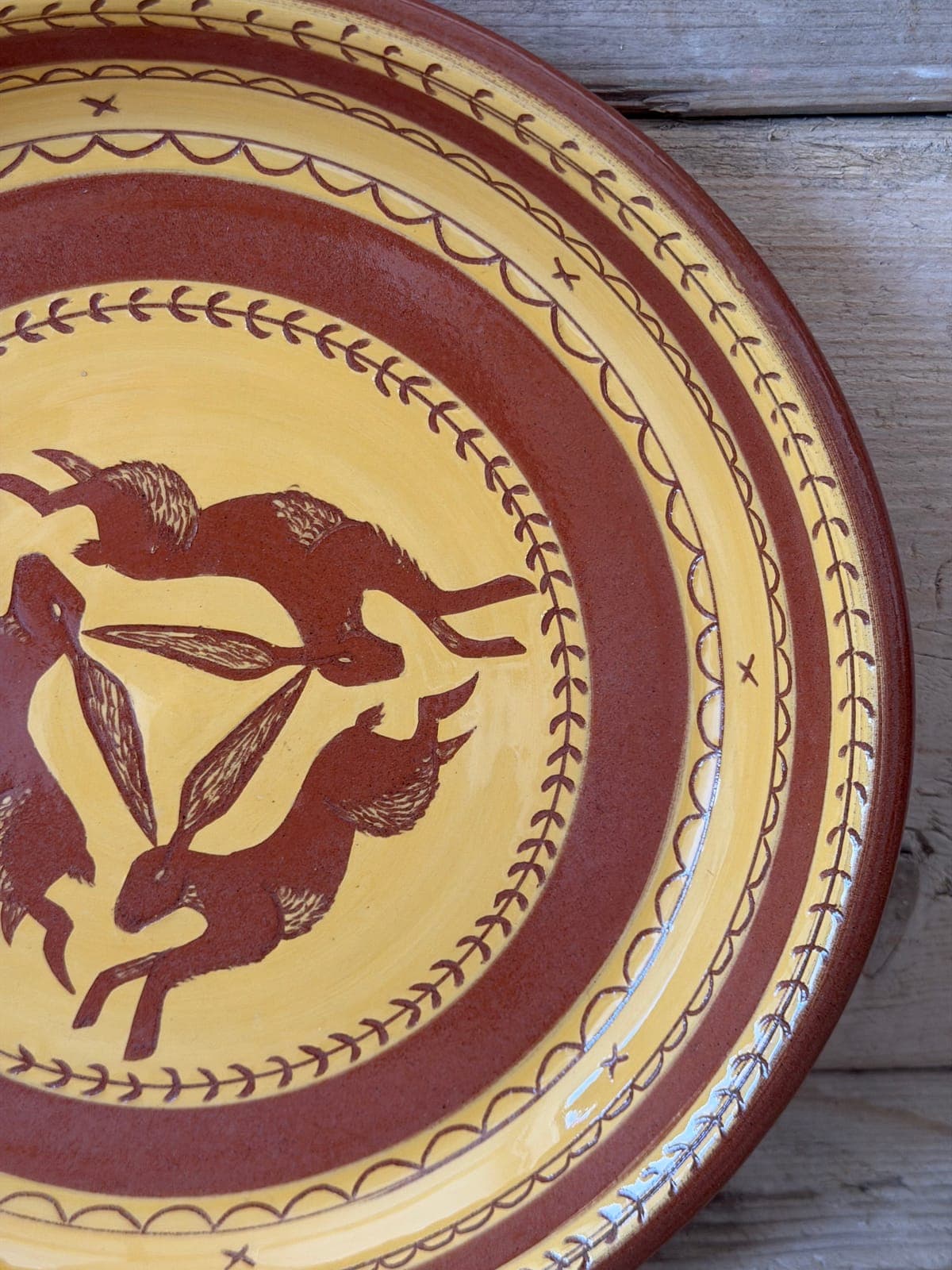 Three hares running in a circle on a yellow and terracotta slipware plate