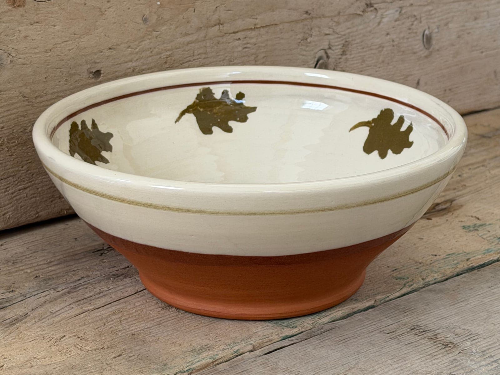 Oak Leaf slipware large bowl in cream slip with olive oak-leaf stamps, sgraffito wavy band and red terracotta foot, on rustic wooden boards